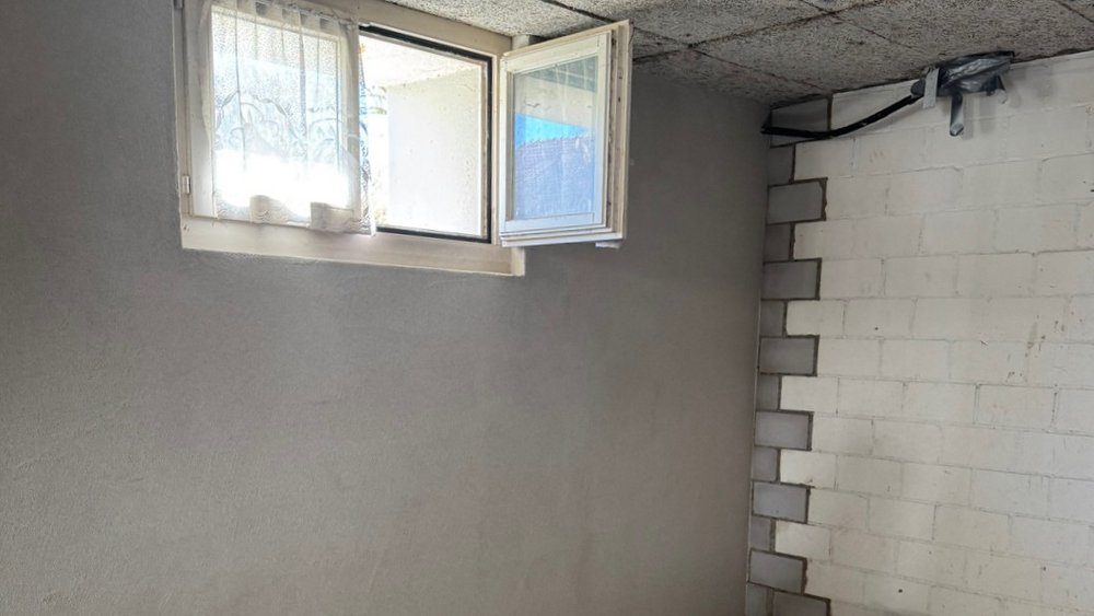 Offenes Kellerfenster über glatter grauer Wand, weiße Steinwand daneben