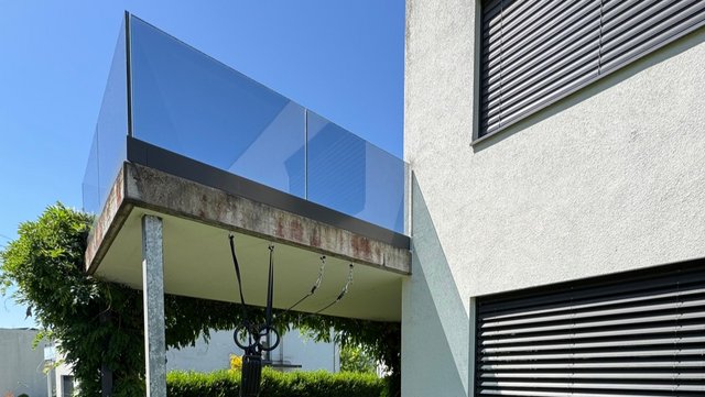 Balkon mit Glasgeländer an Gebäudeecke, Untersicht mit Stützen und sichtbaren Verschmutzungen