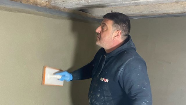 ISOTEC Mitarbeiter glättet beige Masse an Kellerwand