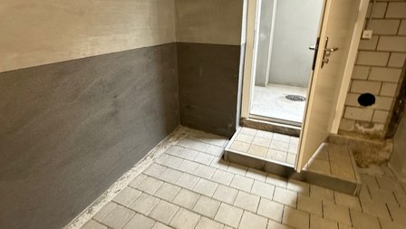 Gefliester Kellerraum mit teils dunkel beschichteter Wand und Türöffnung.