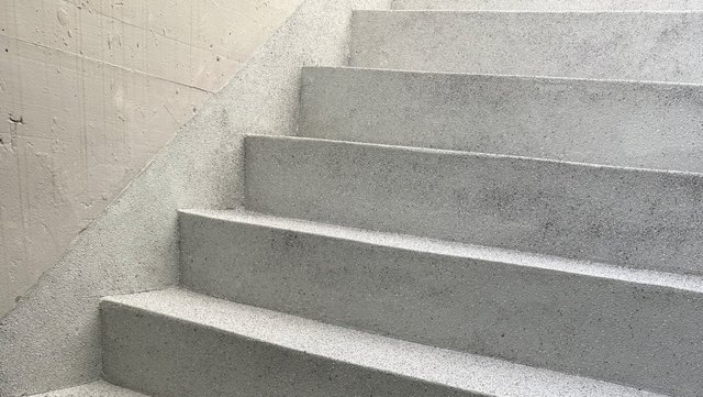 Graue Betontreppe im Treppenhaus, Detailansicht mit rauer Oberfläche.