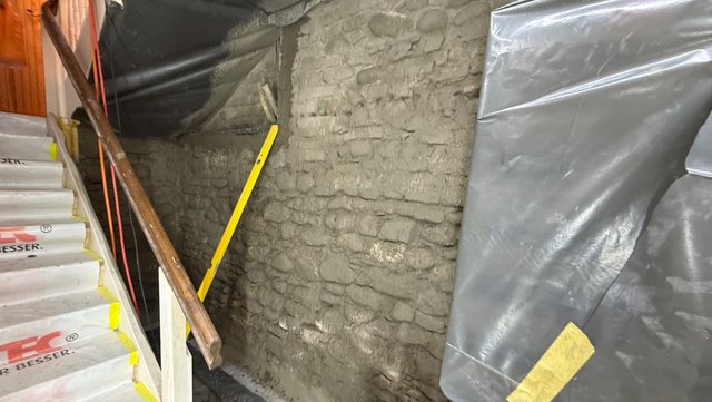 Graue Masse auf freigelegter Ziegelwand im Treppenbereich