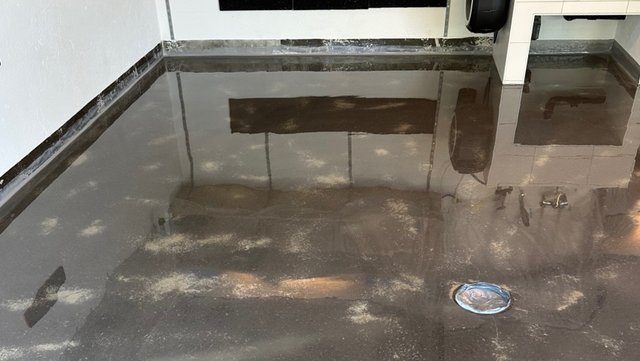 Glänzender dunkler Boden mit stehender transparenter Flüssigkeit und Ablauföffnung im Raum