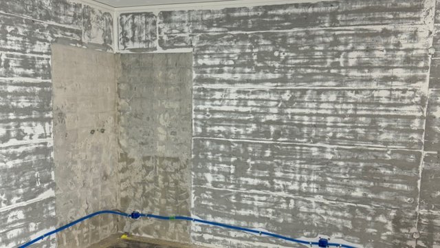 Freigelegte Wand mit grauen Kleberesten im Raum