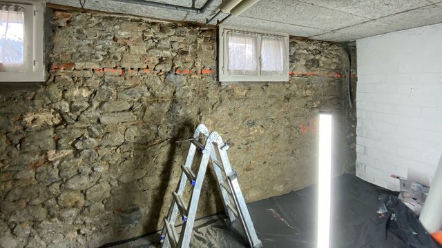 Keller mit freigelegter Natursteinwand, Bohrlöchern und Markierungslinie