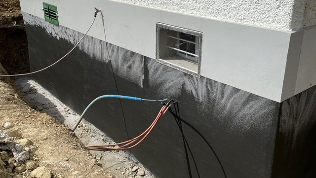 Schwarze Masse auf freigelegter Kellerwand am Gebäude, Leitungen im Graben