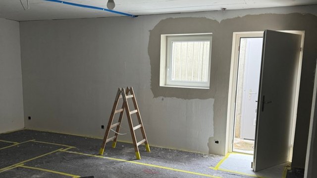 Leiter in renoviertem Raum vor grauer Wand mit Fenster und offener Tür