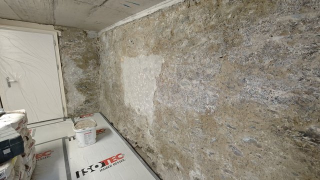 Kellerwand aus Naturstein mit hellgrauer Fläche, Boden mit ISOTEC-Abdeckfolie und Eimer