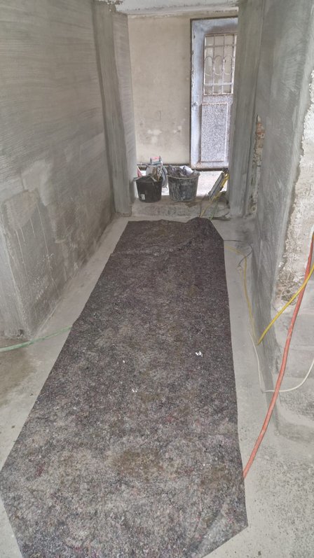 Schmaler Raum mit grauen verputzten Wänden, Schutzvlies und Baueimern