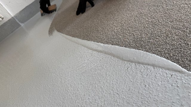 Arbeiter verteilt weiße Masse auf Boden neben Sockelleiste.