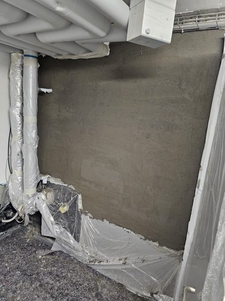 Graue Masse auf Wand aufgetragen, Rohre und Boden sorgfältig mit Folie abgedeckt