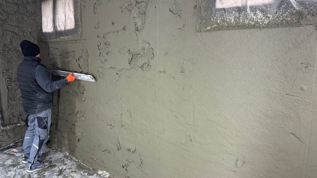 Arbeiter trägt graue Masse auf Wand in unfertigem Raum auf.