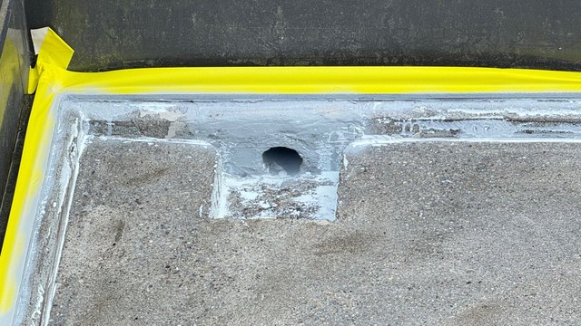 Bohrloch in Betonfläche, graue Masse um Öffnung, gelbes Abklebeband am Rand