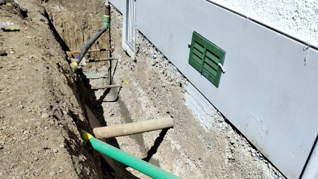 Freigelegte Kellerwand im Erdgraben neben Hausfassade, mit Rohren und Abstützungen