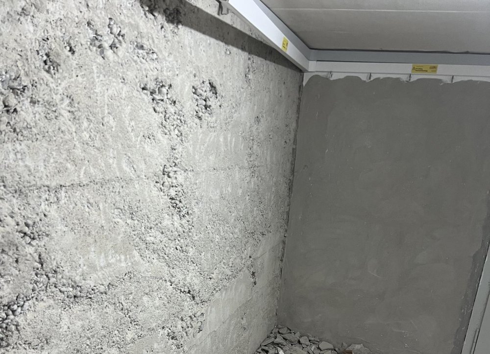 Raue Betonwand neben glatt gespachtelter grauer Wand, Bauschutt am Boden.