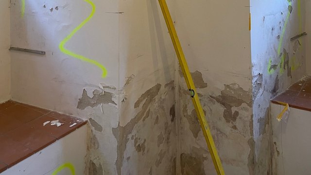 Abgeplatzte Wand mit grauer Masse und Markierungen im Treppenhaus