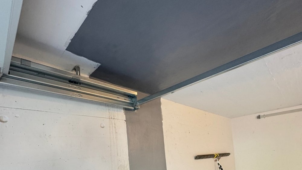 Decke und Wandvorsprung mit grauer Masse bestrichen, daneben Metallschienen