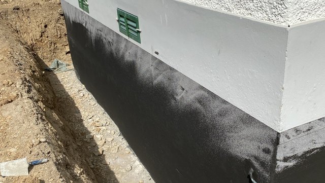 Schwarze Masse auf Kelleraußenwand neben Baugrube aufgetragen