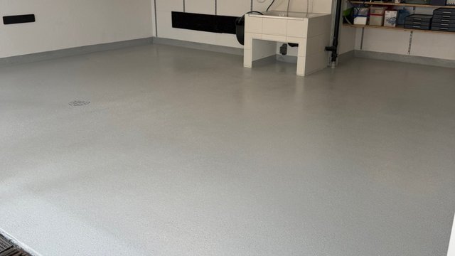 Grauer beschichteter Boden in Kellerraum, Technikgerät und Regale im Hintergrund