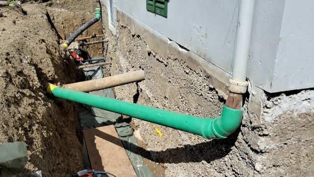 Freigelegte Kellerwand mit gruenem Rohr im Erdgraben am Gebaeude