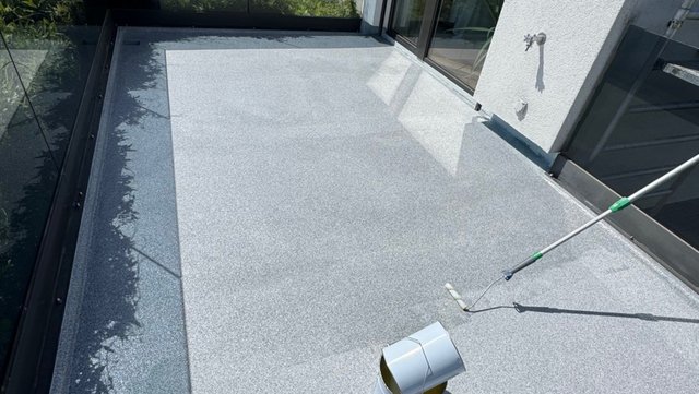 Rolle verteilt transparente Flüssigkeit auf grauem Balkonboden