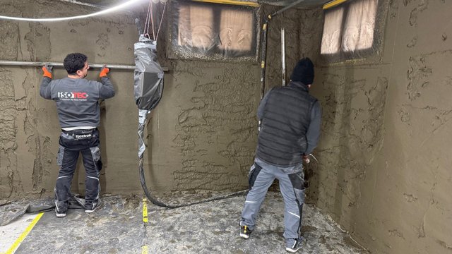 ISOTEC Mitarbeiter glätten graue Masse an Kellerwänden.