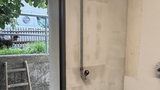 Metallrohr mit Ventil an heller, fleckiger Wand neben offener Tür