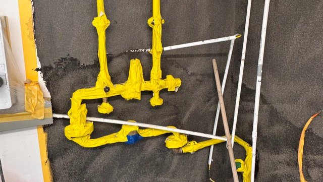 Gelb umwickelte Rohre an schwarzer Fläche, weiße Rohre und Holzstab daneben