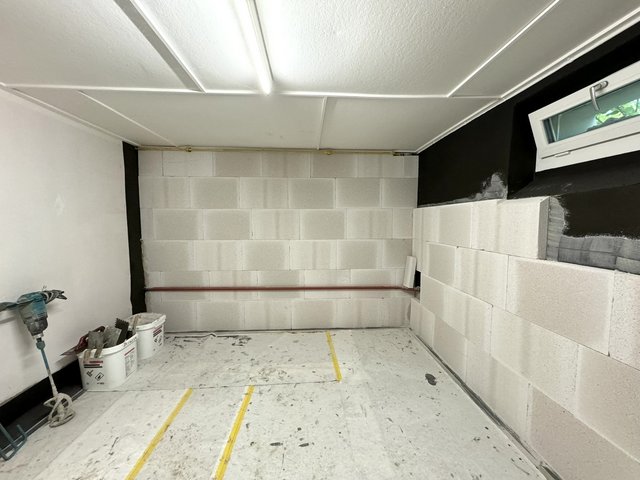 Kellerraum mit hellen Mauersteinen und schwarzer Masse an den Wandkanten, Werkzeuge am Boden