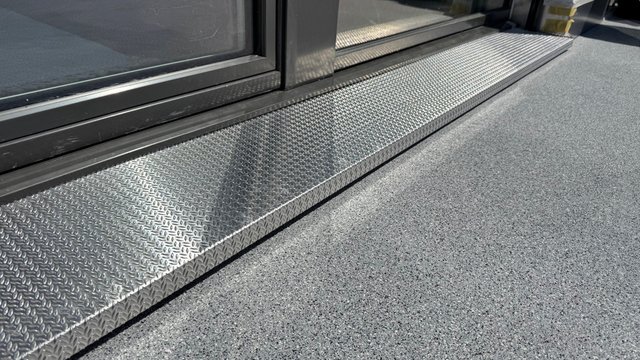 Aluminium-Riffelblech an Türschwelle auf grauem Bodenbelag, Nahaufnahme