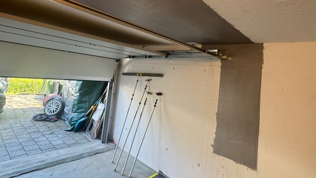Graue Masse als rechteckige Fläche auf Garagenwand neben geöffnetem Tor.
