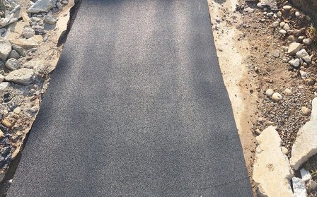 Frisch aufgetragene dunkle Asphaltfläche zwischen Schotterkanten