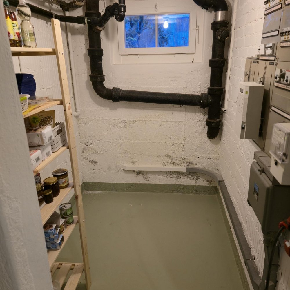 Kellerraum mit schwarzen Rohrleitungen, Fenster und Elektroverteilern an weißer Wand