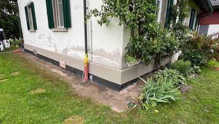 Freigelegter Sockelbereich am Haus mit schwarzer Abdichtung und Erdaushub