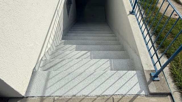 Graue Treppe im Treppenschacht mit blauem Metallgeländer, Draufsicht