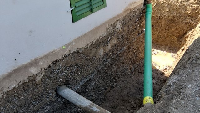 Freigelegte Gebäudewand mit Rohrleitungen im Erdreich neben Fundament