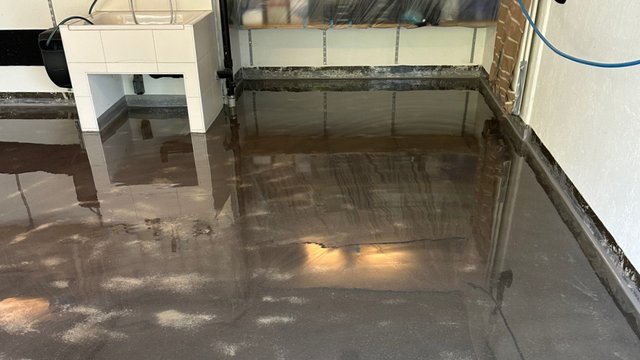 Transparente Flüssigkeit auf Betonboden in Raum, Spiegelungen an Wandkante