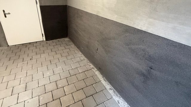 Graue Masse auf Kellerwand, Pflasterboden mit Tür im Hintergrund