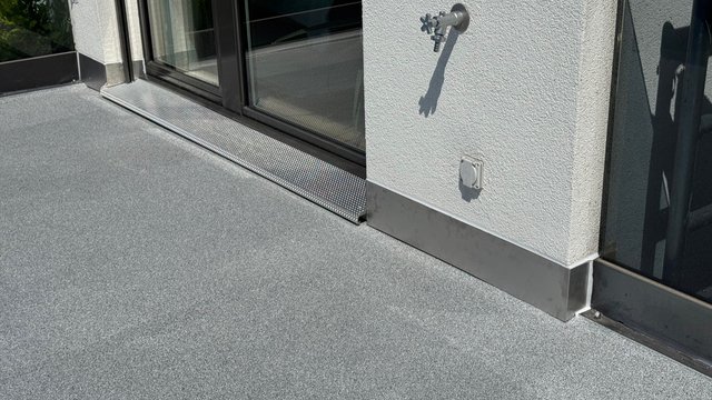 Balkonboden mit grauer Beschichtung, Wandhahn und Steckdose neben Schiebetür