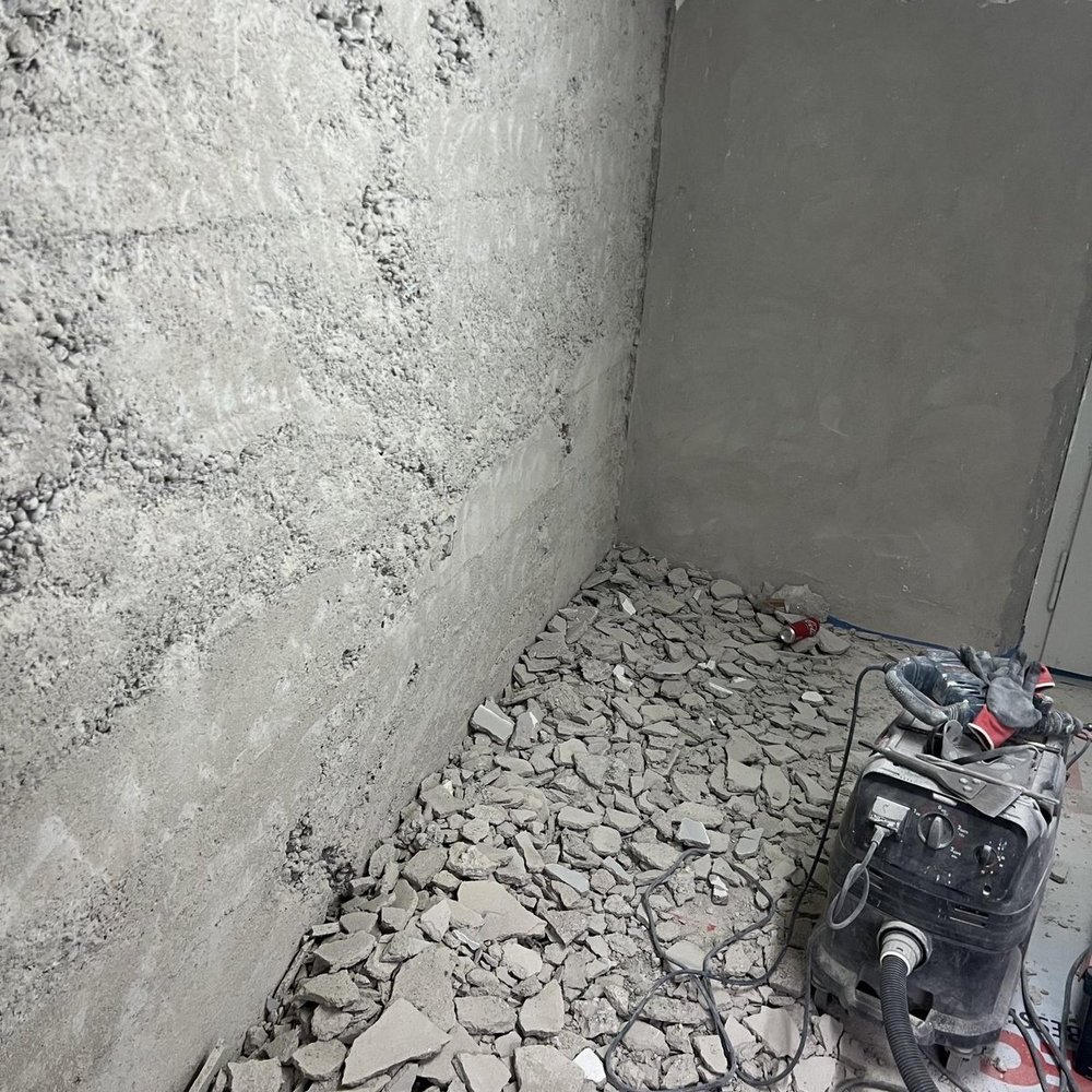 Bauschutt aus grauen Platten auf Boden, graue Wandfläche, Industriesauger im Raum