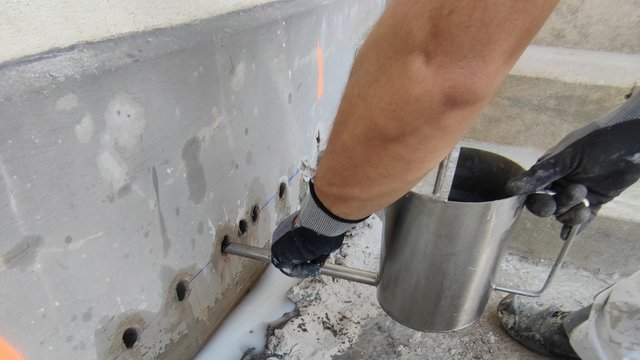 Handschuhhände bedienen Injektionsgerät an Bohrlöchern im Wandbereich.