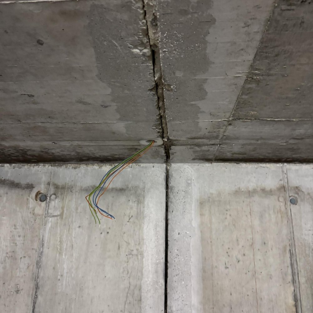 Senkrechte Fuge in Betonfläche, daneben dunkle Feuchteflecken und freiliegende Kabel.