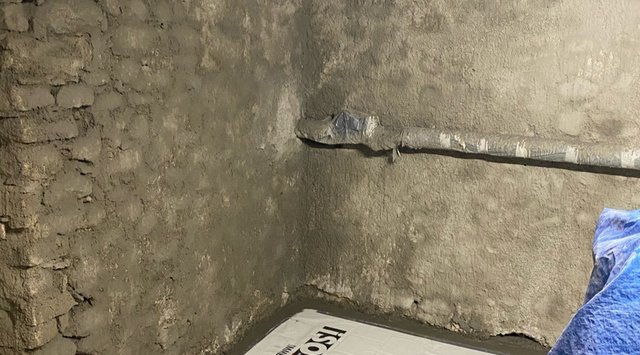 Feuchte Kellerwand mit abblätterndem Putz und provisorisch abgedichtetem Rohr