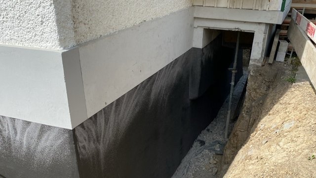 Schwarze Masse auf Kellerwand im Arbeitsgraben aufgetragen