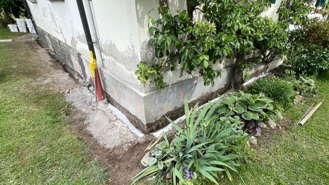 Hausfassade mit Bohrlochreihe am Sockel und weißer Flüssigkeit im Graben