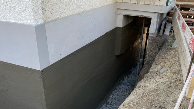 Freigelegte Gebäudewand mit dunkler Masse im Erdreich beschichtet