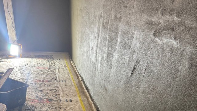 Rauhe graue Wand in Raum mit abgedecktem Boden und Baustrahler.