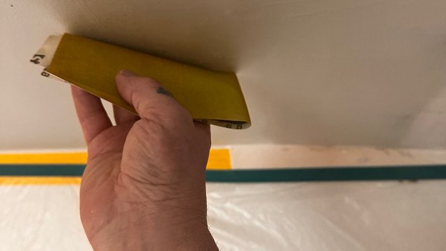 Hand schleift Deckenfläche mit gelbem Schleifklotz, Folie am Boden