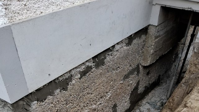 Freigelegte Kellerwand mit heller Dämmplatte und grober grauer Masse im Erdreich