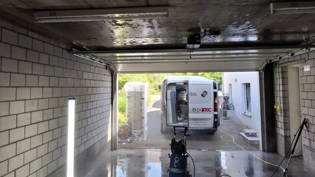 ISOTEC Transporter steht vor offener Garage, nasser Betonboden mit Kabeltrommel und Geräten.